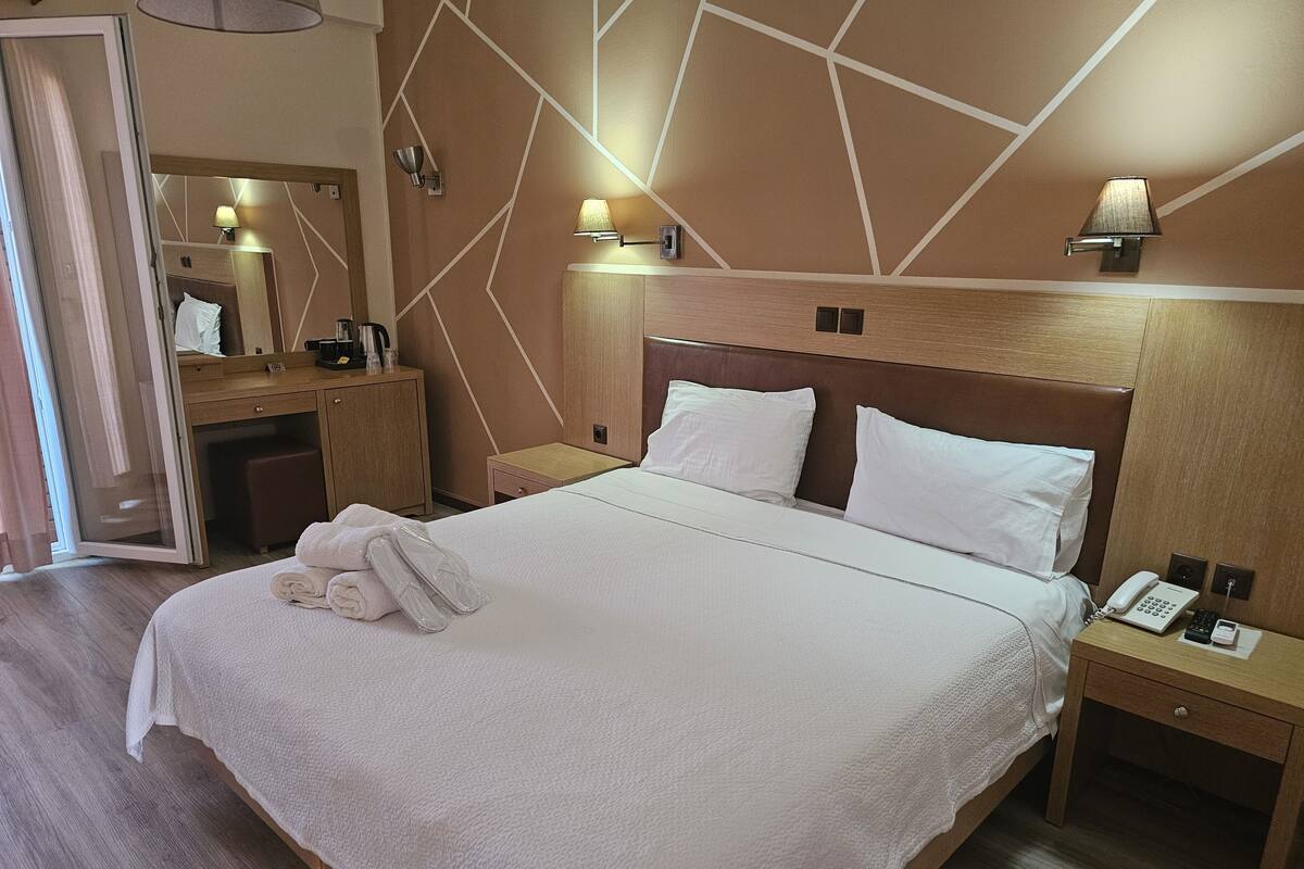 Un lit bien fait, avec du linge de lit blanc, une table de chevet avec un téléphone et une lampe, et une petite table en bois servant de table de nuit, également avec une lampe.