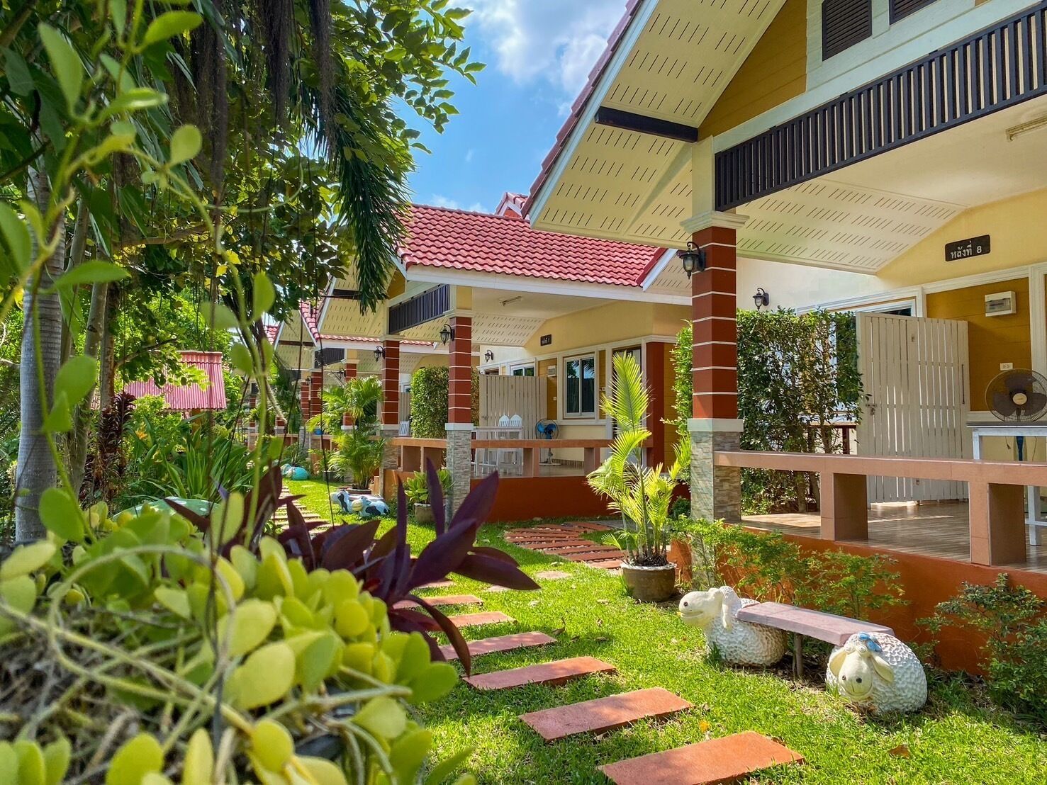 A hotel with a red-tiled roof, multiple balconies, and a well-maintained garden with stepping stones and various plants.
