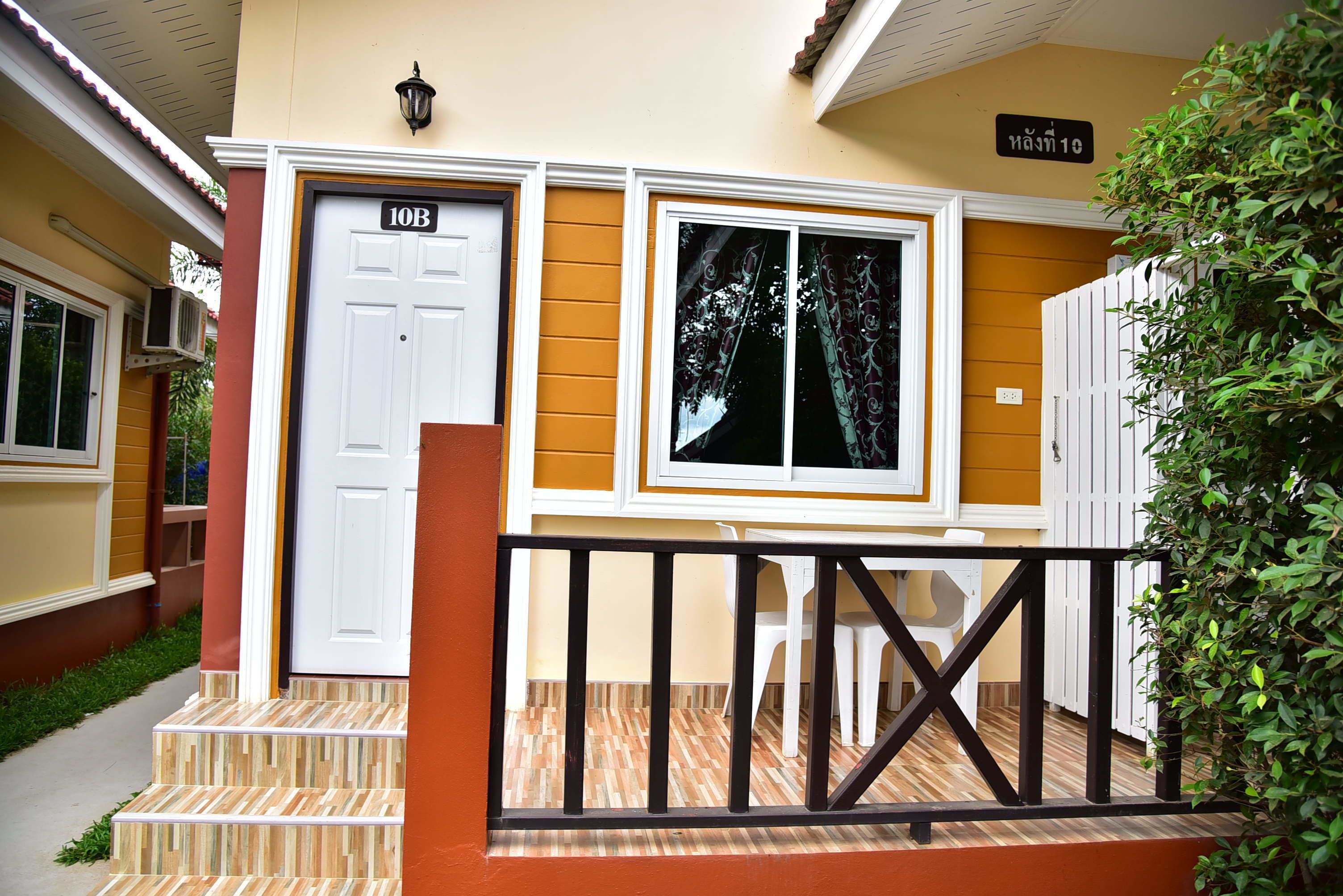 A house with a number 10B sign, a white door, a window with a tree view, and a small porch with a railing.