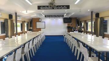 Una sala de conferencias con mesas largas y sillas blancas, un reloj y una pantalla de televisión en la pared.