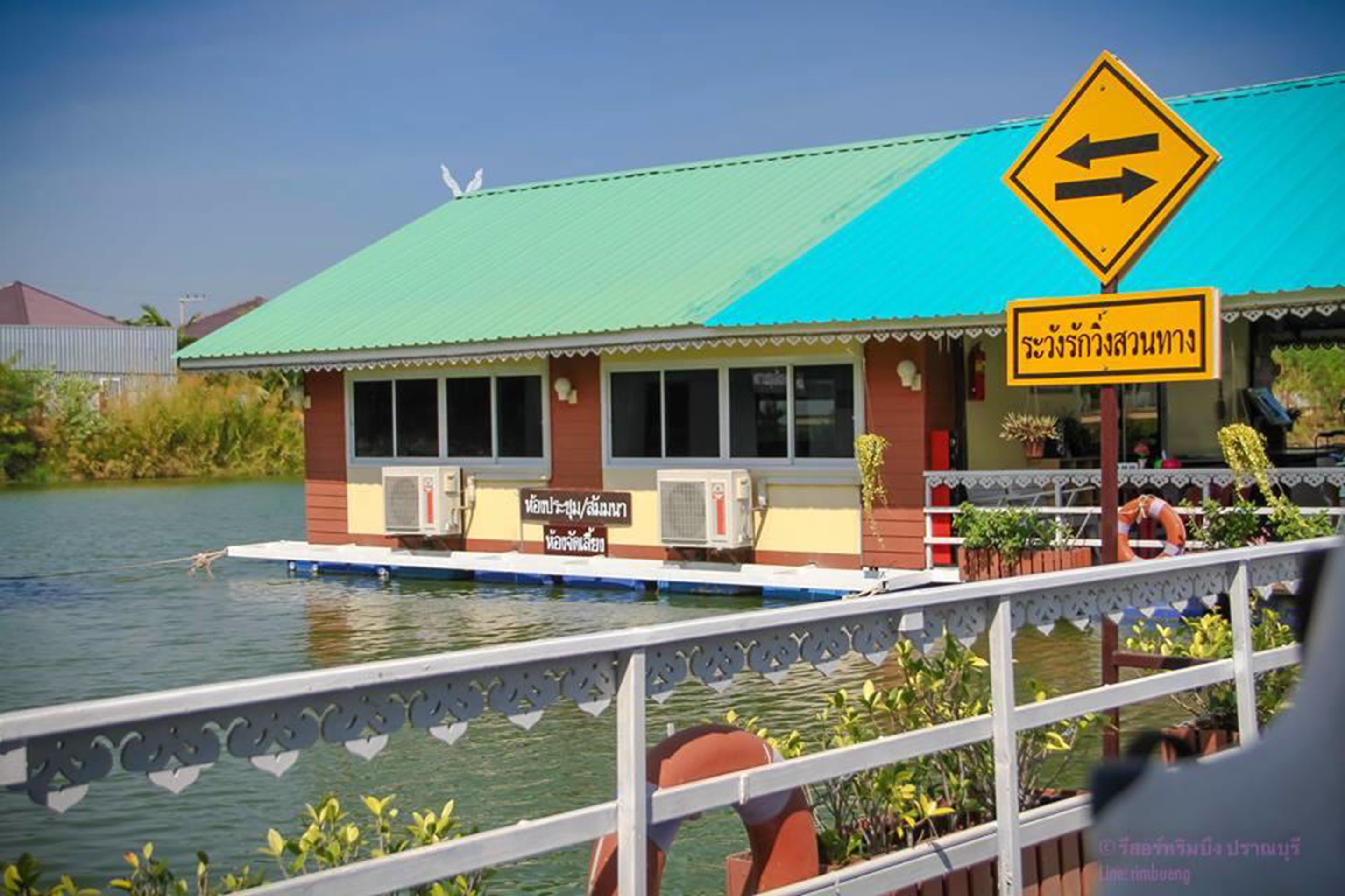 A floating house with a green roof, air conditioning units, and a sign in a foreign language.