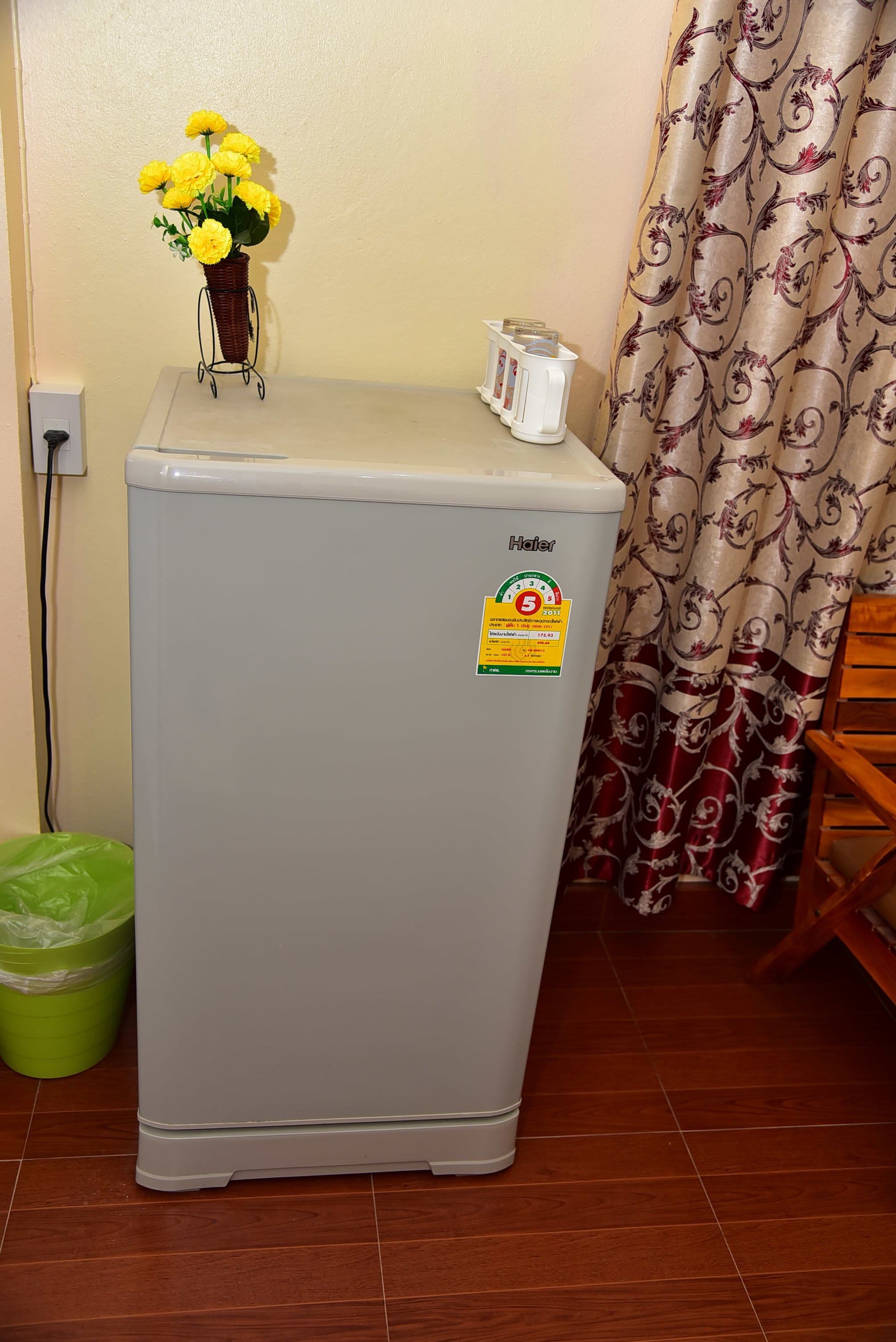 A compact refrigerator with a sticker, a basket of yellow flowers, a white container, and a green trash bin.