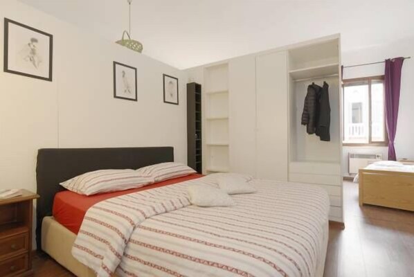 A bedroom with a bed, a nightstand, a wardrobe, and a window with curtains.