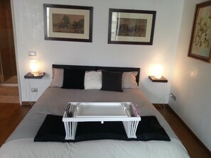 A neatly made bed with a white headboard, two bedside tables with lamps, and two framed pictures on the wall. - Bonadies Suite (Barletta)
