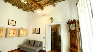 Una sala de estar con un sofá gris, suelo de madera, techo con vigas a la vista y un reloj de madera grande.