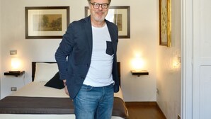 Un hombre de pie en una habitación de hotel con una cama, mesitas de noche y cuadros en las paredes.