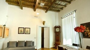 Una habitación con techo de madera, un sofá, una mesa de comedor con sillas, un reloj y un cuadro en la pared.