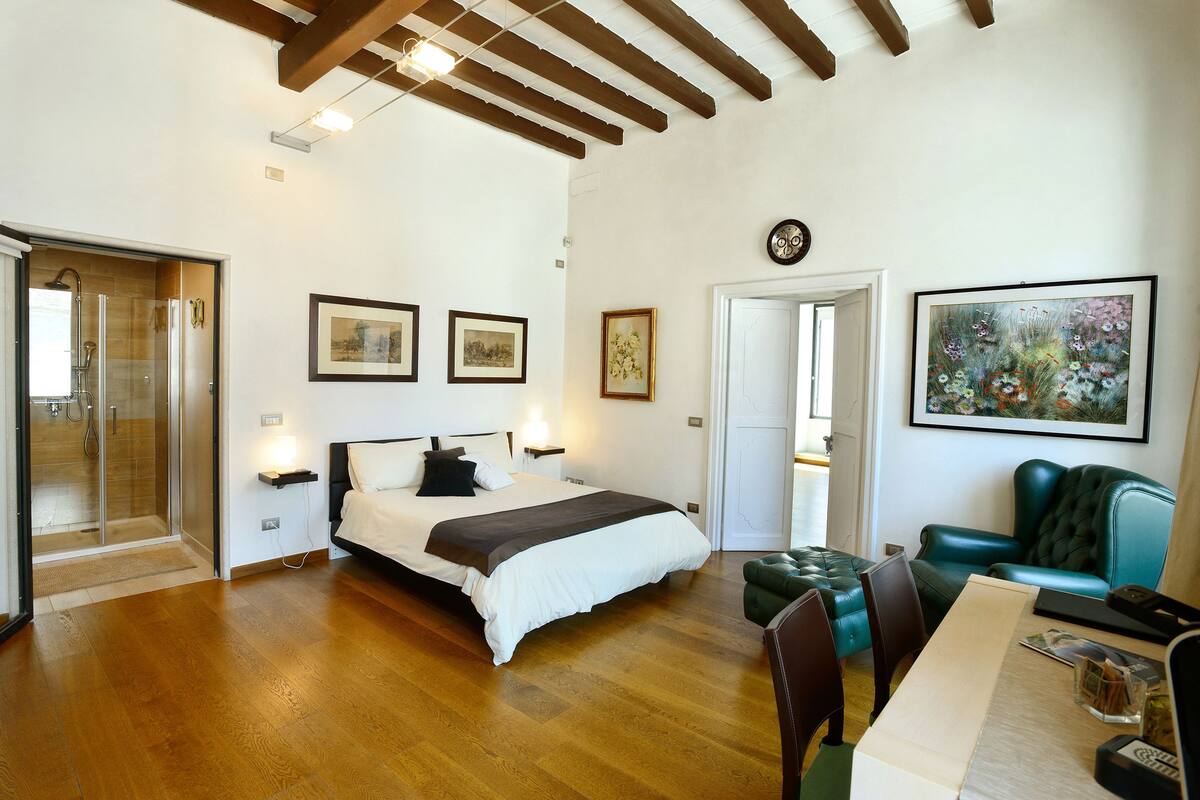 A spacious bedroom with a large bed, a sitting area with a green leather chair, and a dining table.