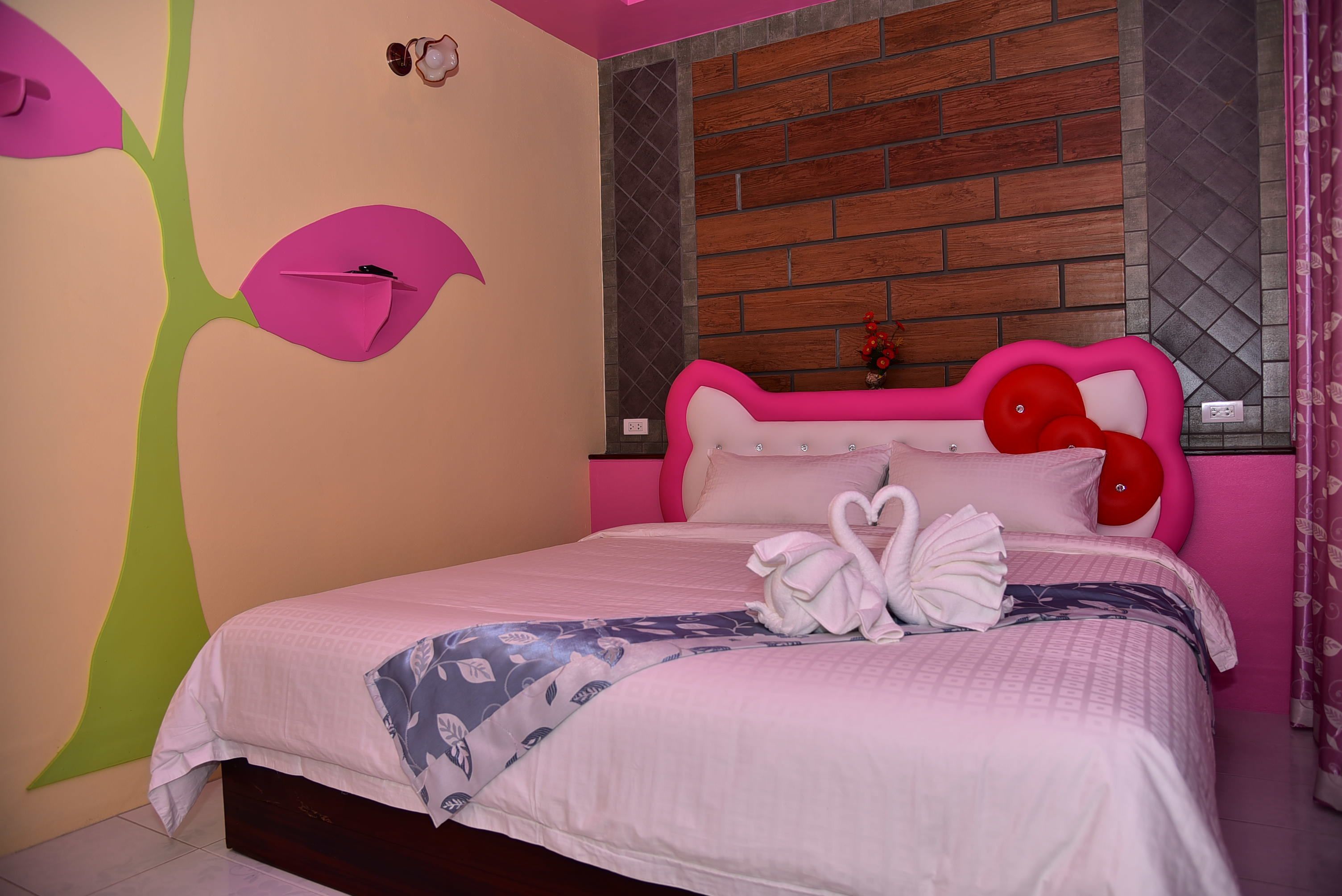 A bedroom with a pink and green wall mural, a brick-patterned headboard, and a bed with pink bedding and red balloons.