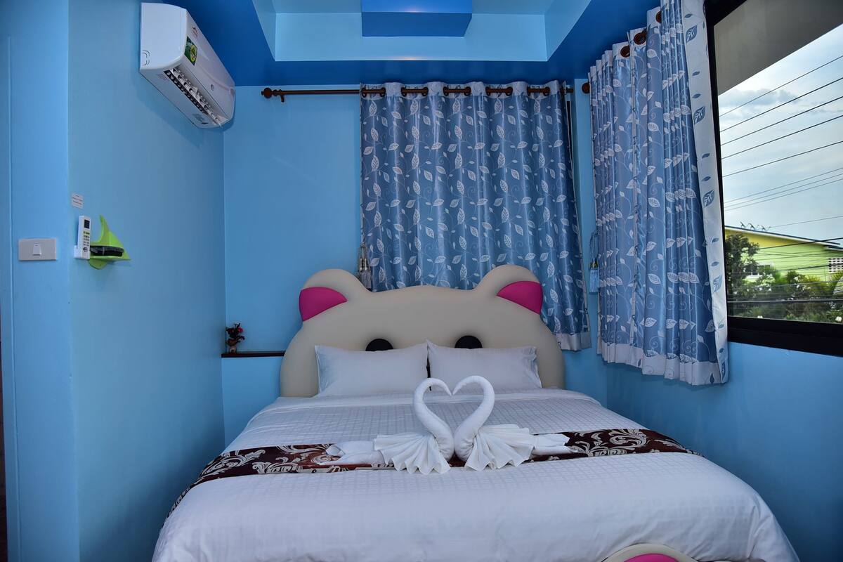 Un dormitorio con pared azul, cama con cabecera blanca y cortinas con estampado de hojas.
