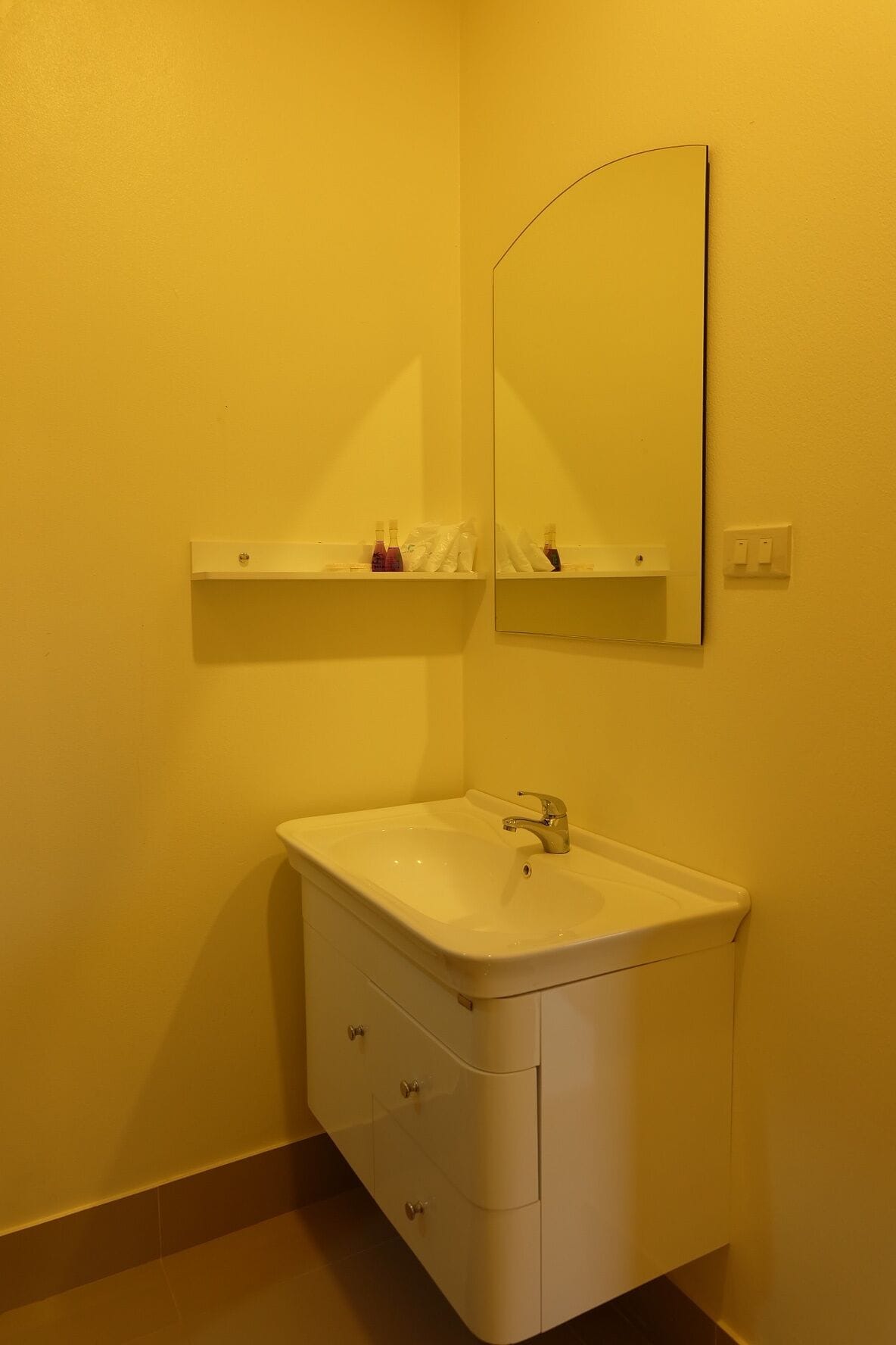 A bathroom with a white sink, a mirror, and a shelf above the sink.