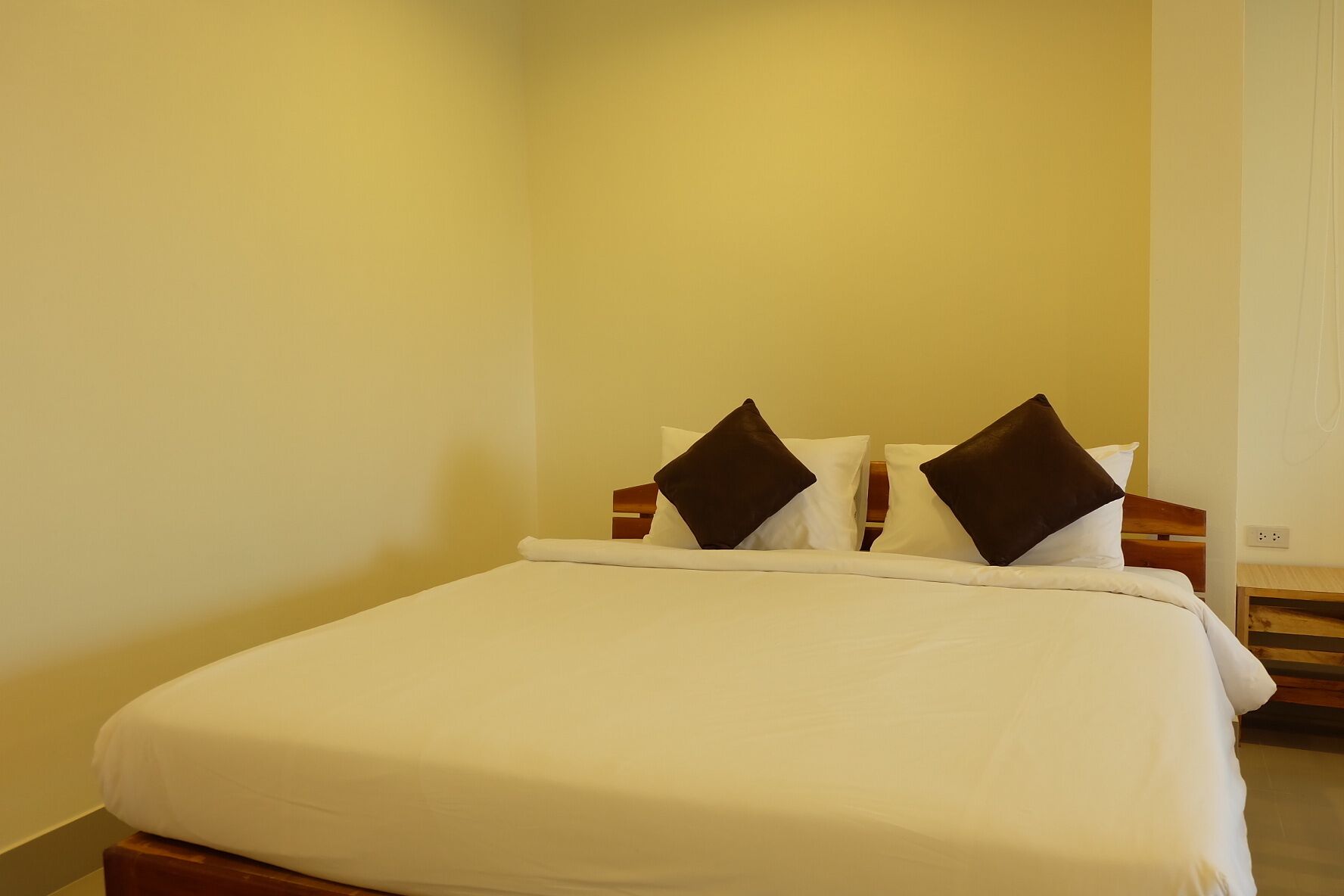 A neatly made bed with white bedding and two dark brown pillows.