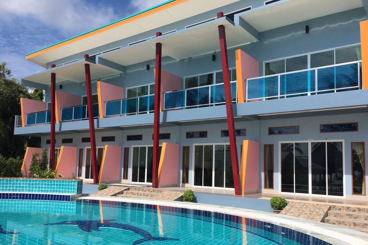 A modern hotel with a pool, featuring a two-story structure with balconies, large windows, and a clear view of the pool area.
