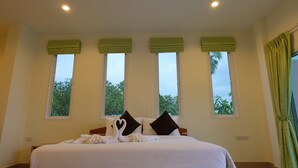 Ein Hotelzimmer mit einem großen Bett, vier Fenstern mit grünen Jalousien und Blick ins Grüne.