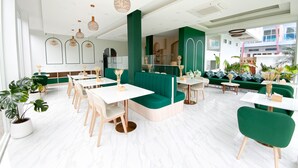 Ein modernes Restaurant mit grünen Sitzflächen, weißen Tischen und Pendelleuchten.