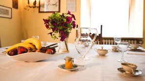 A dining table with a bowl of fruit, a vase of flowers, a pitcher, and tea cups. - Villa Liberty B&B (Fano)