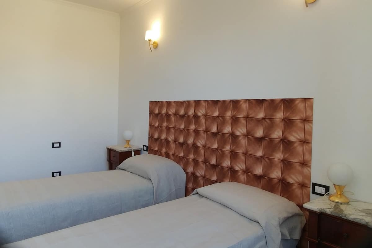 A bedroom with two beds, a tufted headboard, bedside lamps, and a nightstand with a lamp.