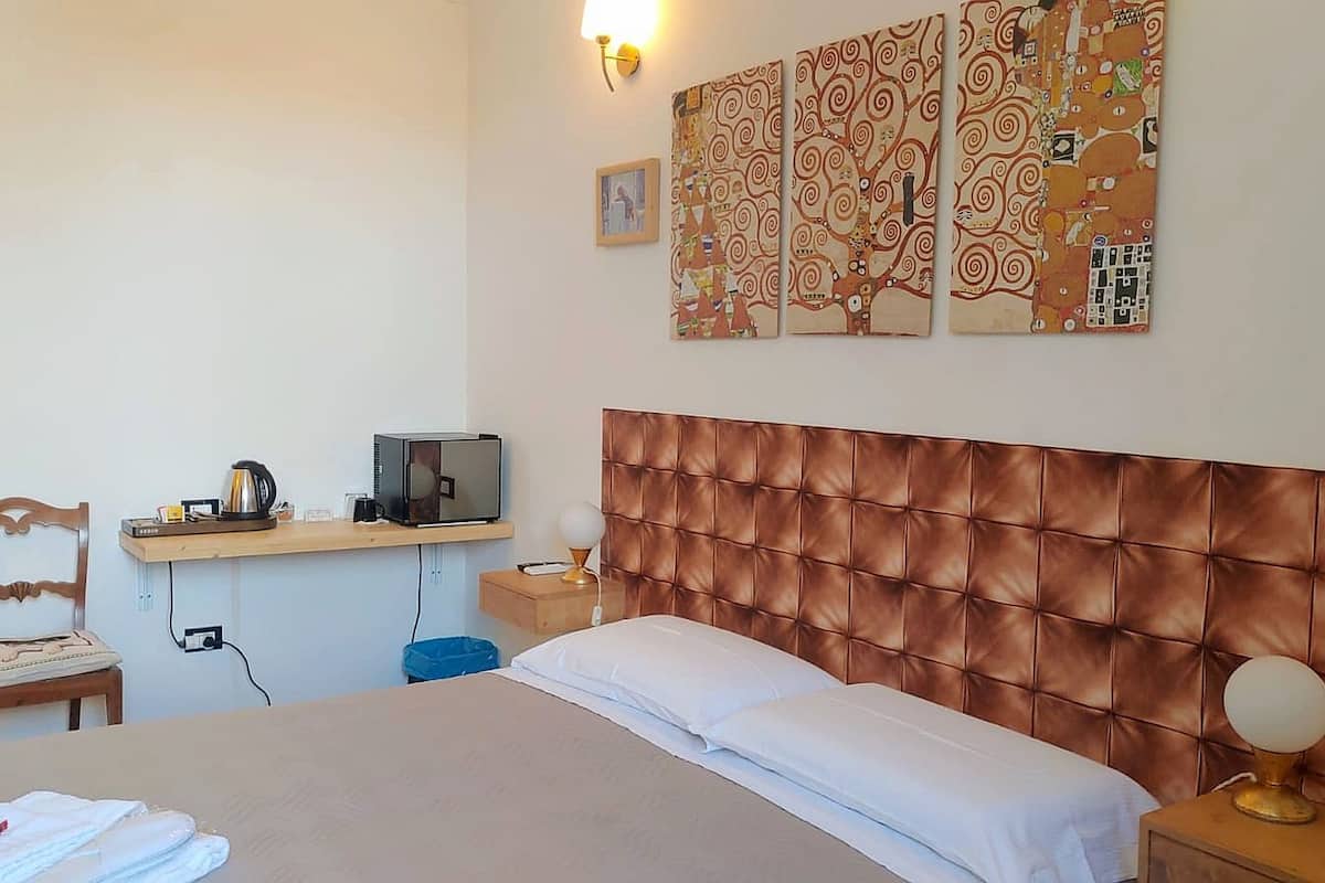 A hotel room with a bed, a desk with a computer, a chair, and a wall with artwork.