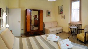 A hotel room with a bed, a sofa, a chair, a small table, a mirror, and a TV. - Villa Liberty B&B (Fano)