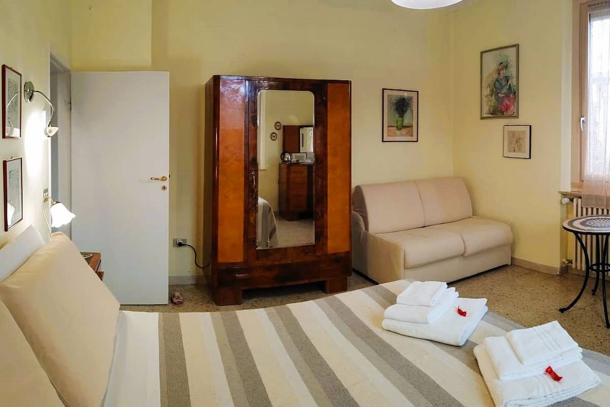 A hotel room with a bed, a sofa, a chair, a small table, a mirror, and a TV.