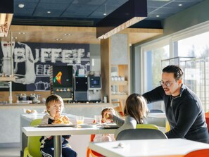 A dining area with tables, chairs, and a person standing. - Ibis Budget Brugge Jabbeke (Jabbeke)