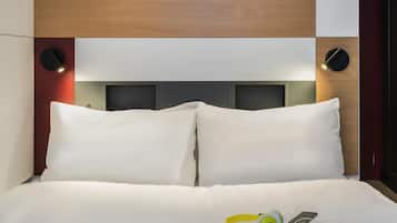 Een hotelkamer met een houten hoofdbord, twee witte kussens, een bed met een witte dekbedovertrek en een koptelefoon op het bed.