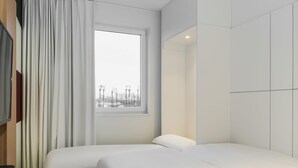 Une chambre d’hôtel moderne dotée d’une grande fenêtre, d’un lit, d’une télévision et d’une armoire.