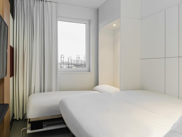 A modern hotel room with a large window, a bed, a TV, and a wardrobe. - Ibis Budget Brugge Jabbeke (Jabbeke)