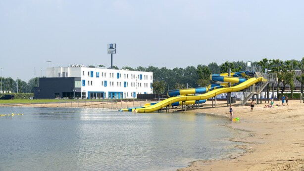 Une plage avec un toboggan aquatique, un bâtiment doté de nombreuses fenêtres et un ciel dégagé.