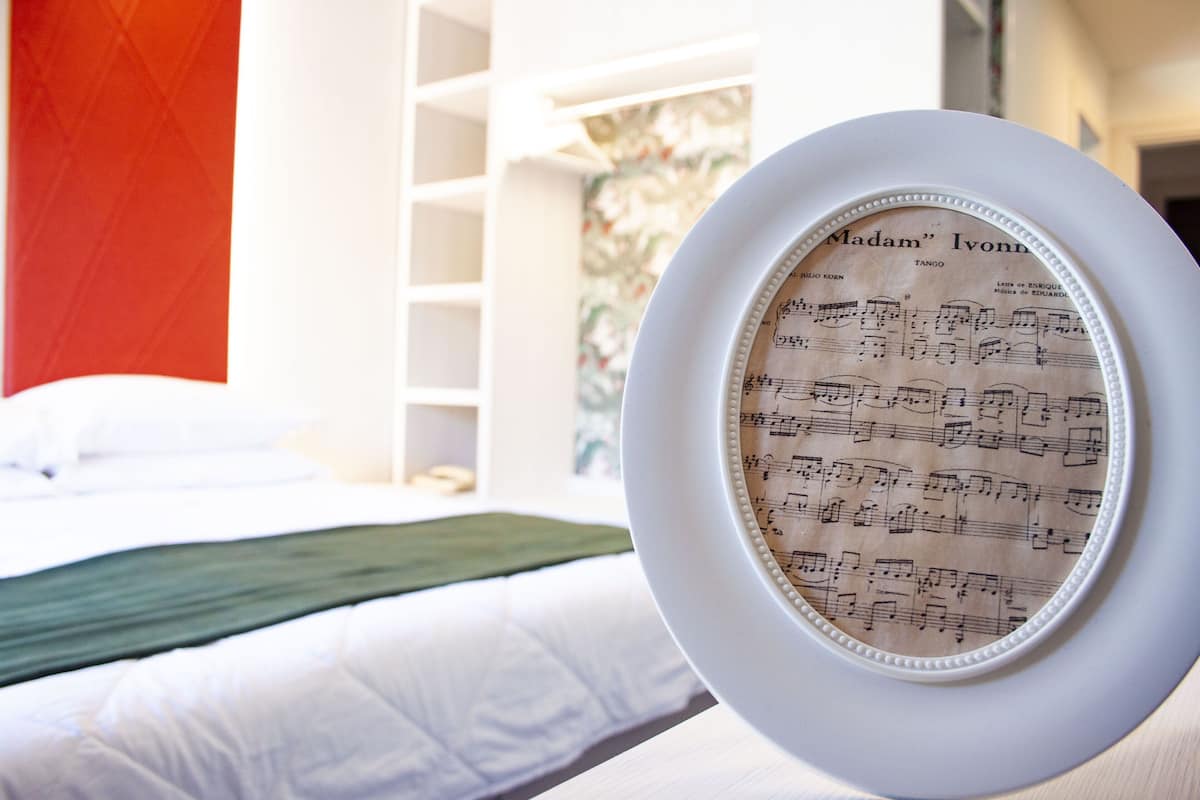 A framed sheet music titled "Madam Ivonna" in a hotel room with a bed and a white wall.