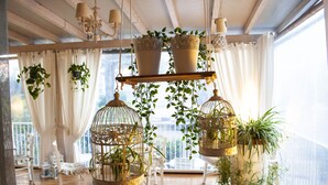 A room with hanging planters, white chairs, and a view through large windows. - Hotel Loretta & Dependance (Cervia)