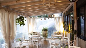 A covered patio area with white furniture, potted plants, and a view of the outdoors. - Hotel Loretta & Dependance (Cervia)