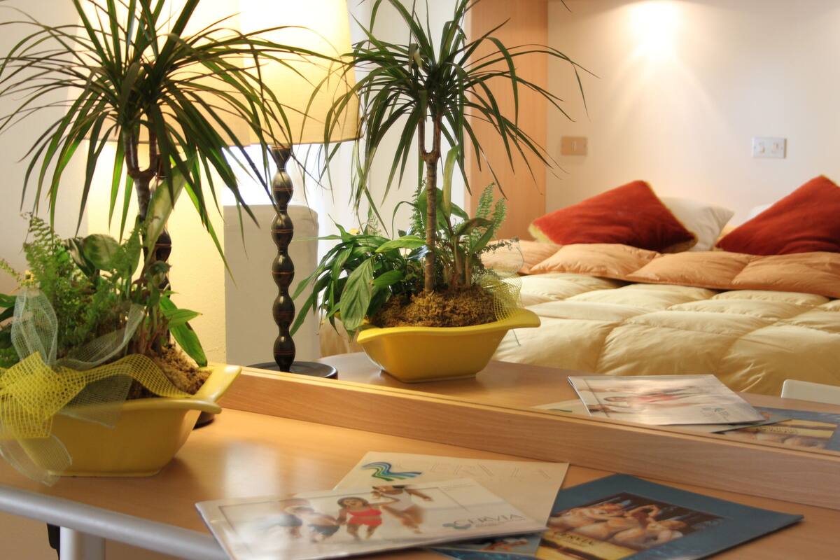 A bedroom with a bed, pillows, and two potted plants on a bedside table.