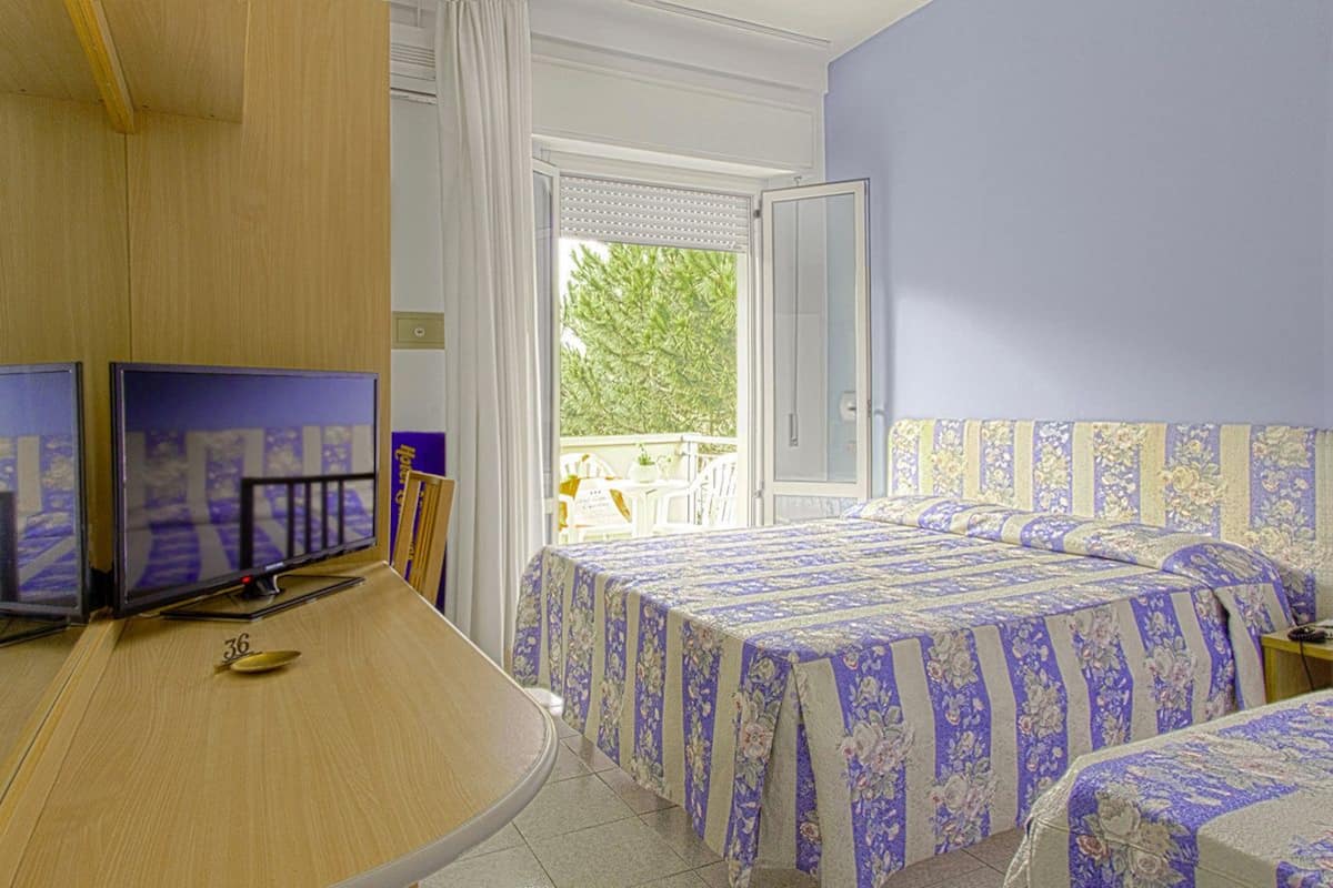 A hotel room with two beds, a desk with a computer, and a window with a view of greenery.