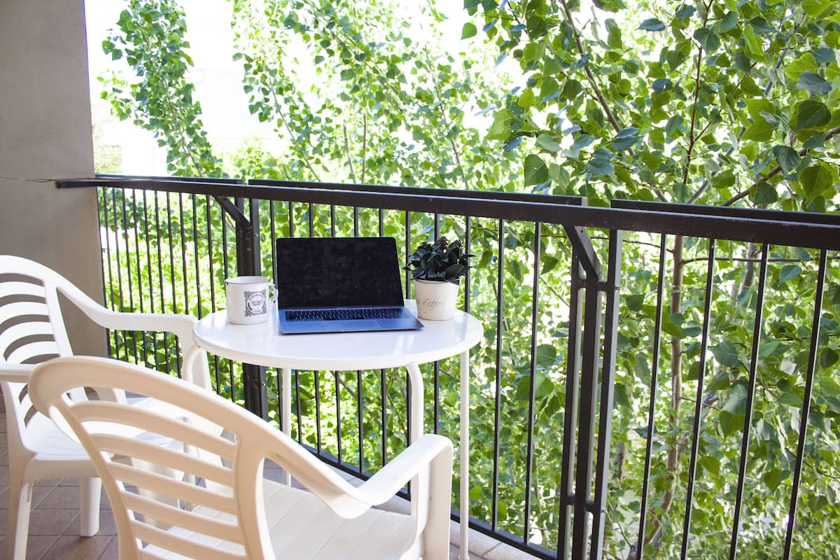 A balcony with a white table, a laptop, and a potted plant.