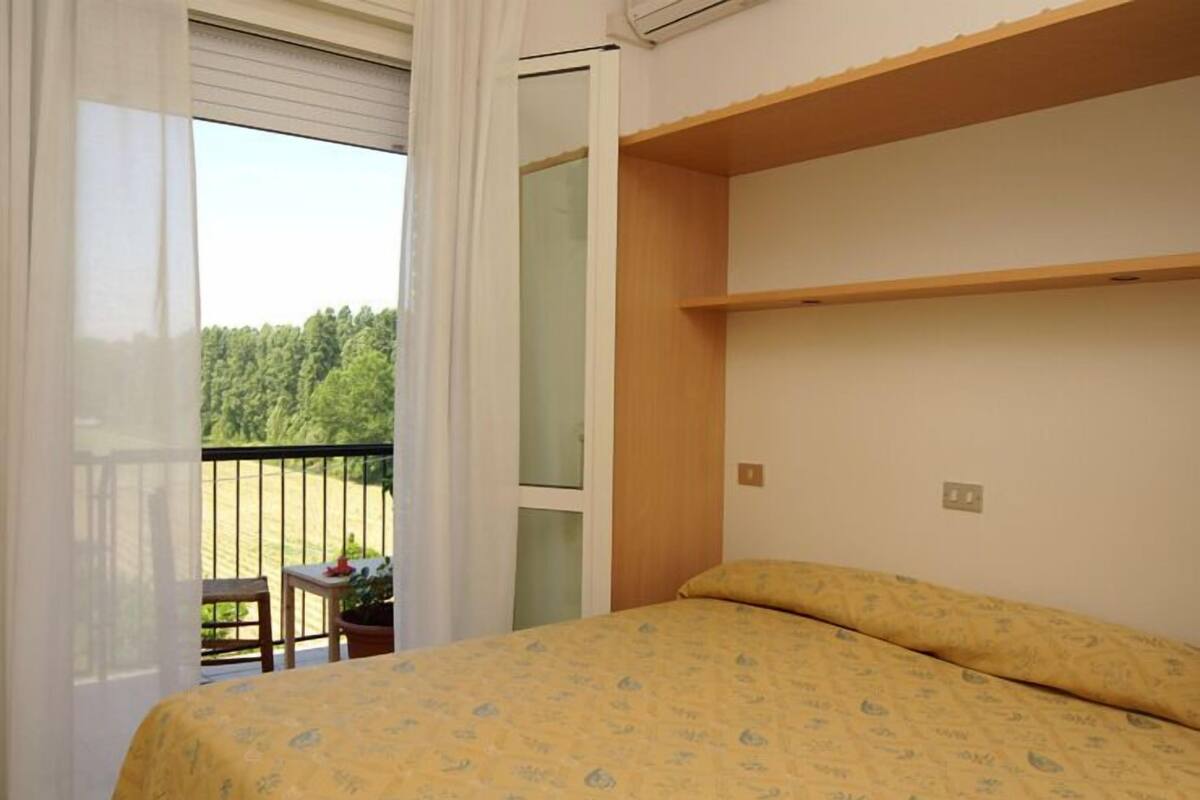 A bedroom with a bed, a wooden shelf, a window, and a balcony with a table and chair.