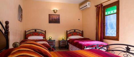A bedroom with two beds, a wall-mounted air conditioner, a painting, and a window with curtains.