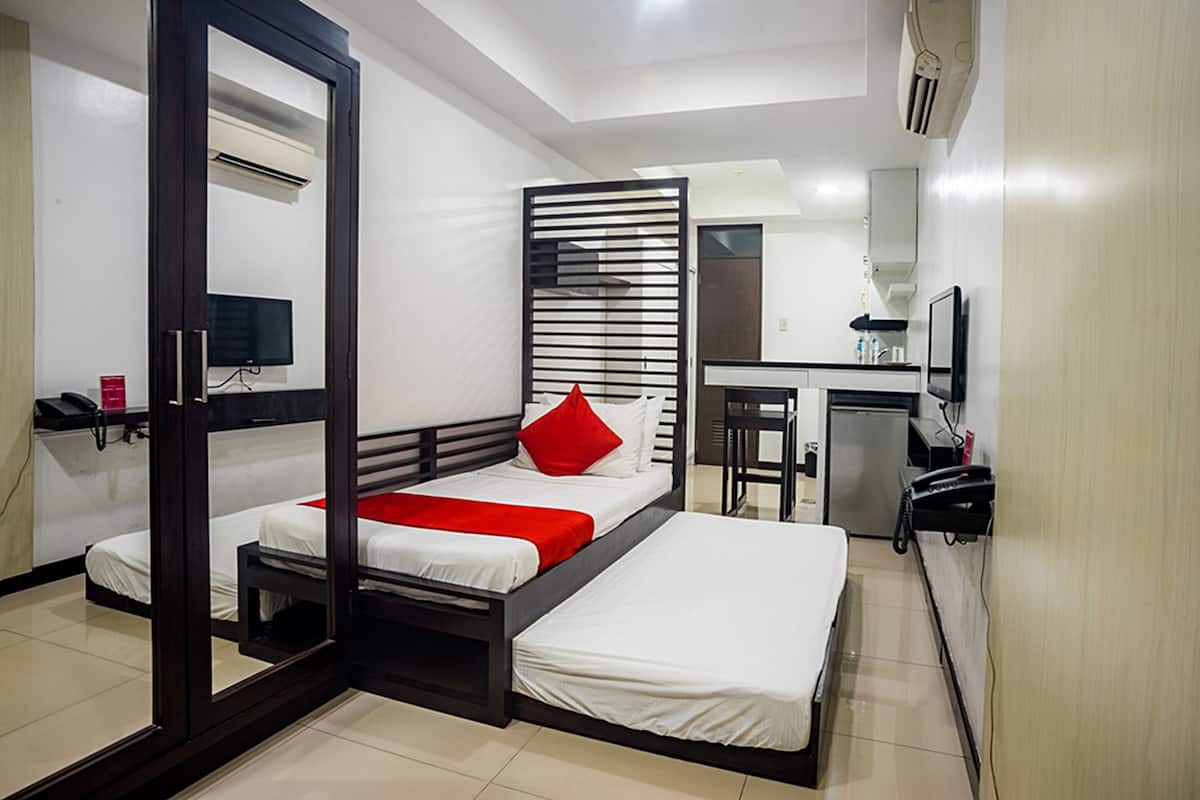 A compact hotel room with two beds, a desk, a mirror, and a kitchenette.
