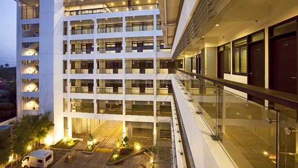 A multi-story hotel with a modern design, featuring a central courtyard with plants and a parking area. - Copenhagen Main Residences (Mandaue)