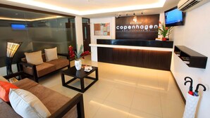 A modern hotel reception area with a reception desk, seating area, and a television mounted on the wall. - Copenhagen Main Residences (Mandaue)