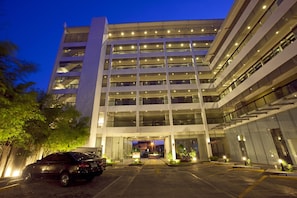 Un hotel moderno con diverse altezze, dotato di un ampio parcheggio e un ingresso ben illuminato.