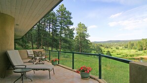 A balcony with outdoor furniture, a view of a forest, and a distant landscape.