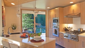 A modern kitchen with a central island, stainless steel appliances, and a view of greenery outside.