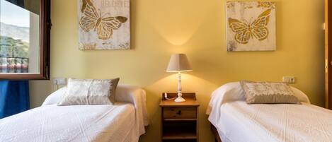 A hotel room with two beds, a nightstand, a lamp, and two butterfly-themed wall art pieces.