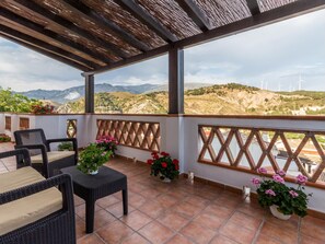 A covered outdoor seating area with wicker furniture and potted plants, overlooking a mountainous landscape with wind turbines. - Fabulous villa with private pool and views (Cónchar)