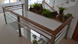 A modern indoor space with a glass railing, wooden floor, and a variety of plants arranged on a white surface.