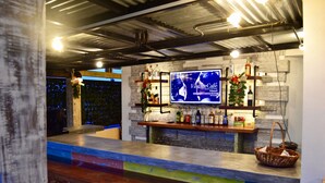 A bar area with a television displaying 'Vintage Café' and shelves with bottles and a Christmas tree.