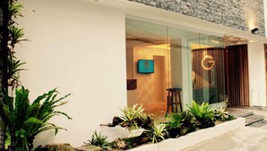 A modern building with a glass entrance, a logo on the wall, and a stone wall behind.