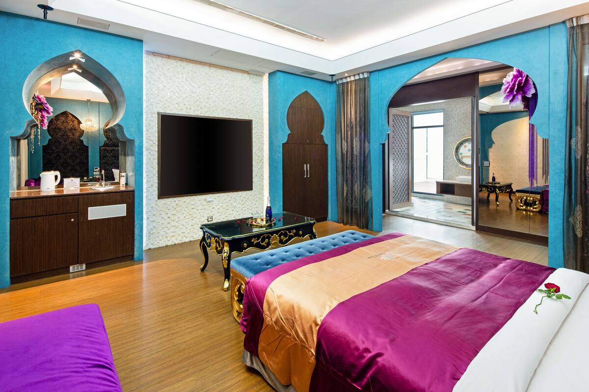 Ein modernes Hotelzimmer mit einem großen Bett, einem Flachbildfernseher, einem Schminktisch mit Spiegel und einer Holzkommode.
