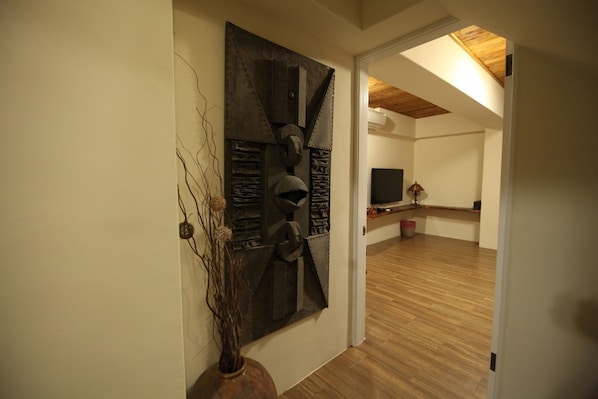 A hallway with a modern abstract wall art piece, a wooden floor, and a television in the background.